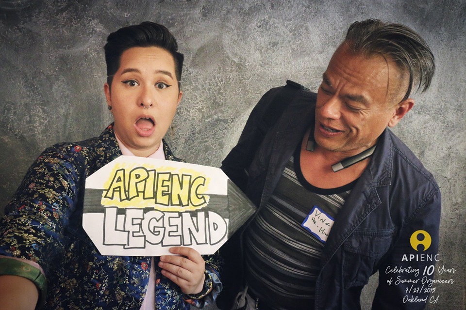 Image description: Sammie is holding a sign that says "APIENC Legend" with an arrow pointing to Vince. Vince is looking down at the sign.