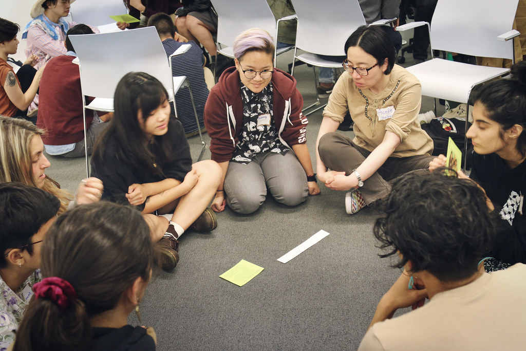 Image description: A group of TGNC API people and allies sit on the floor in a circle.
