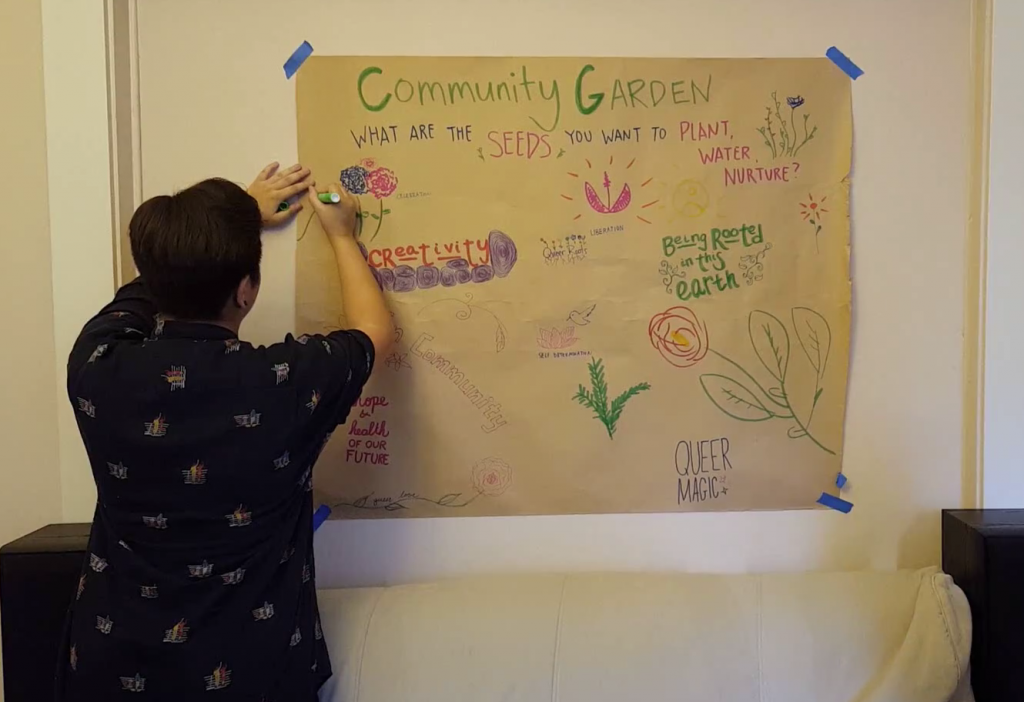 Image description: A large portion of butcher paper is taped onto a wall indoors and reads "Community Garden." There are illustrations of plants and descriptive words. Sammie is on the left drawing on the paper.