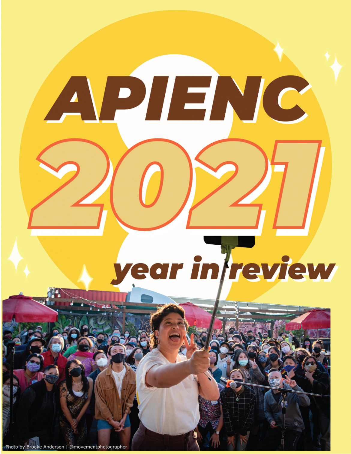 Image description: On a light yellow background in front of a large APIENC circle logo reads “APIENC 2021 year in review”. Below is a picture of a large crowd of masked QTAPIs smiling and posing at a camera.”
