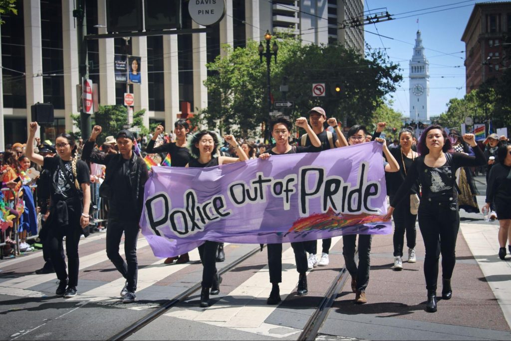 Image description: Lavender Phoenix members dressed in black with a “Police Out of Pride” banner
