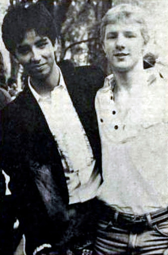 Image of Kenji at 18, in 1980, black hair, brown eyes, Asian ‘mixed race,’ wearing a white ruffled shirt, and a black dress jacket with his arm over the shoulder of his former highschool boyfriend, Buddy Frasier, blonde hair wearing a white ruffle shirt too, at the Boston “Gay Pride March” with a total number of marchers @ 5,000 people. Buddy passed in 1995 due to AIDS