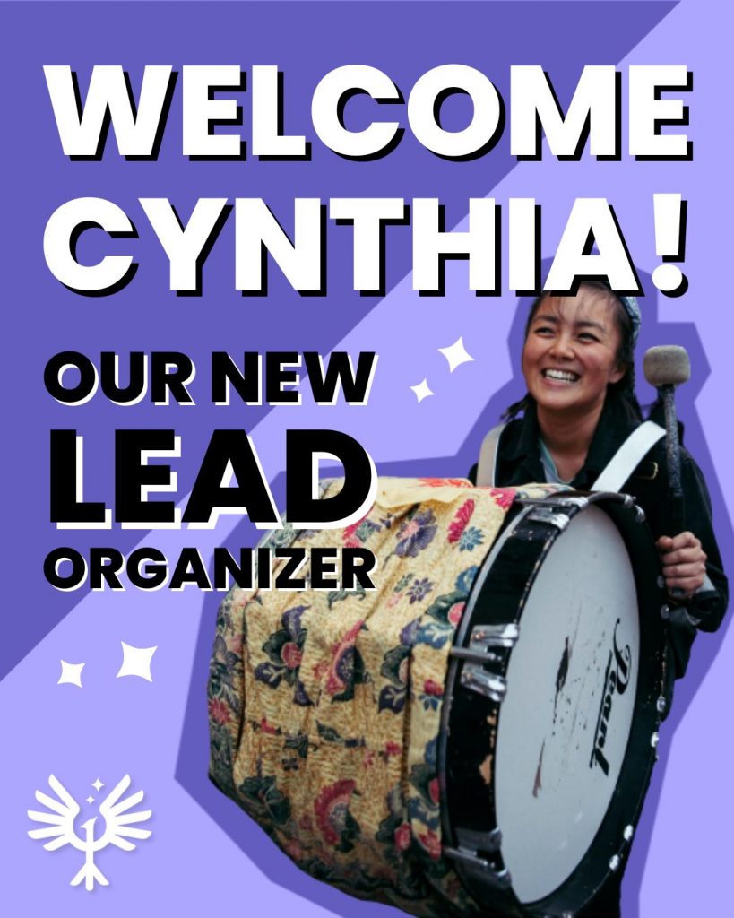 Image description: on a purple background bold text says "WELCOME CYNTHIA! OUR NEW LEAD ORGANIZER" and Cynthia smiles while playing a large drum strapped to their shoulders and marching.