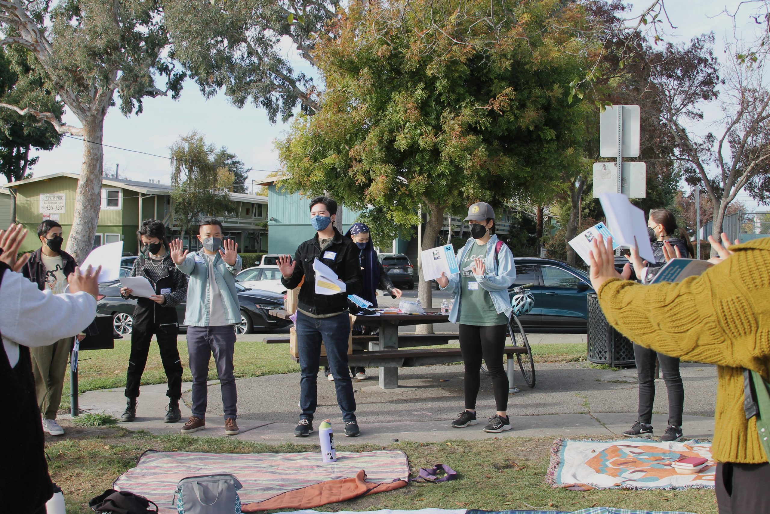 Image description: A group of masked TQAPIs are in a community room facing the front where there is a facilitator speaking to the group.