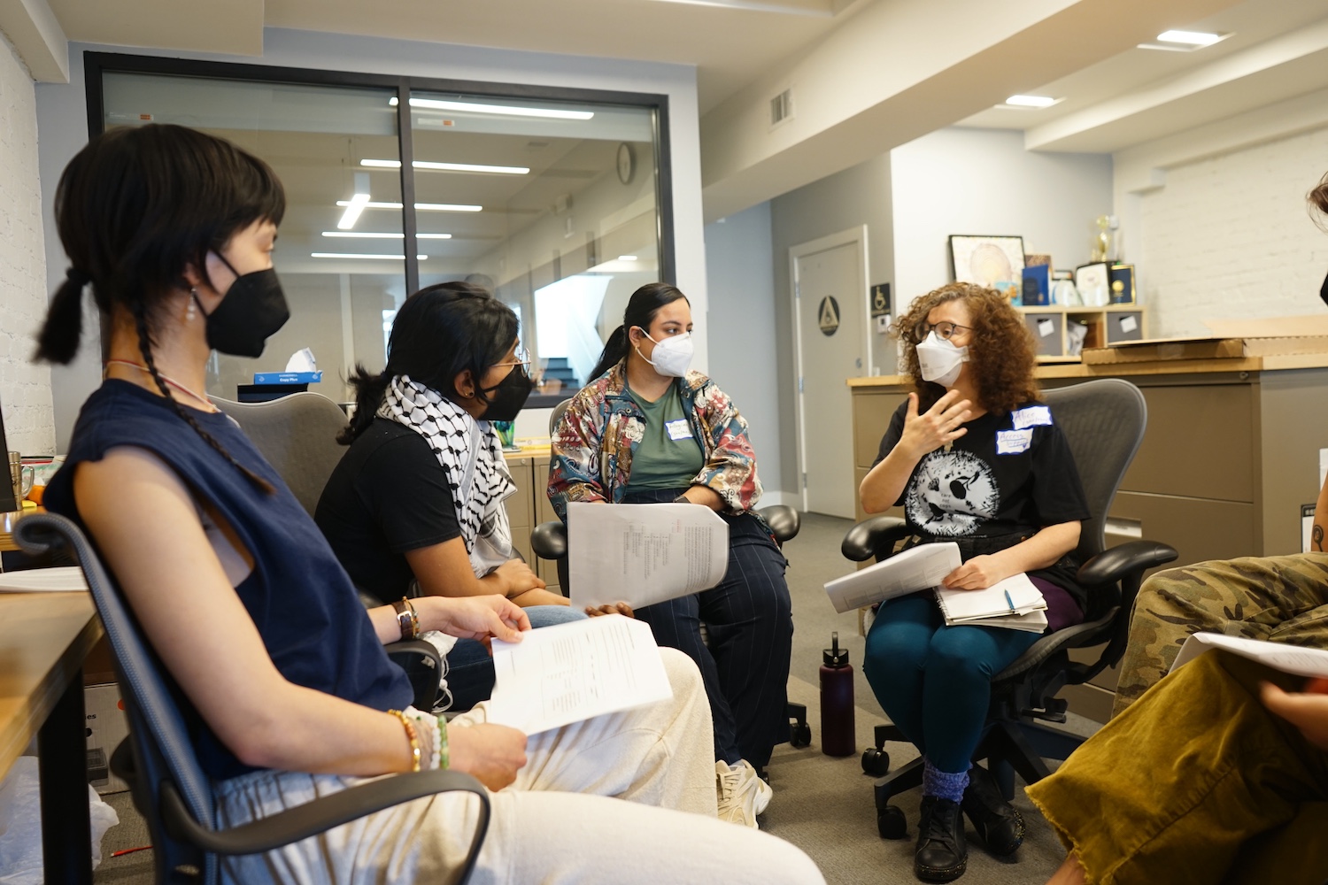 Image description: A group of masked TQAPIs are indoors sitting in a circle.