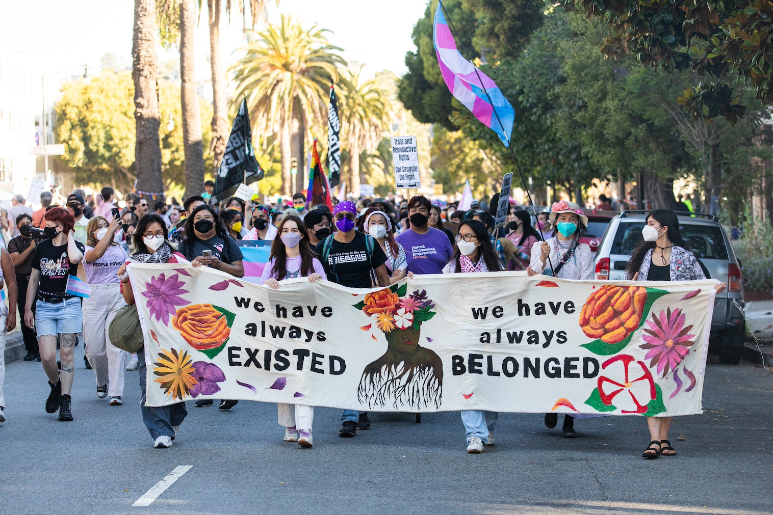 Image Description: A group of masked trans and queer Asian and Pacific Islander people hold a large purple banner that reads: Police Out of Pride. There is a black banner to the left that reads BLACK LIVES MATTER in multiple different languages.