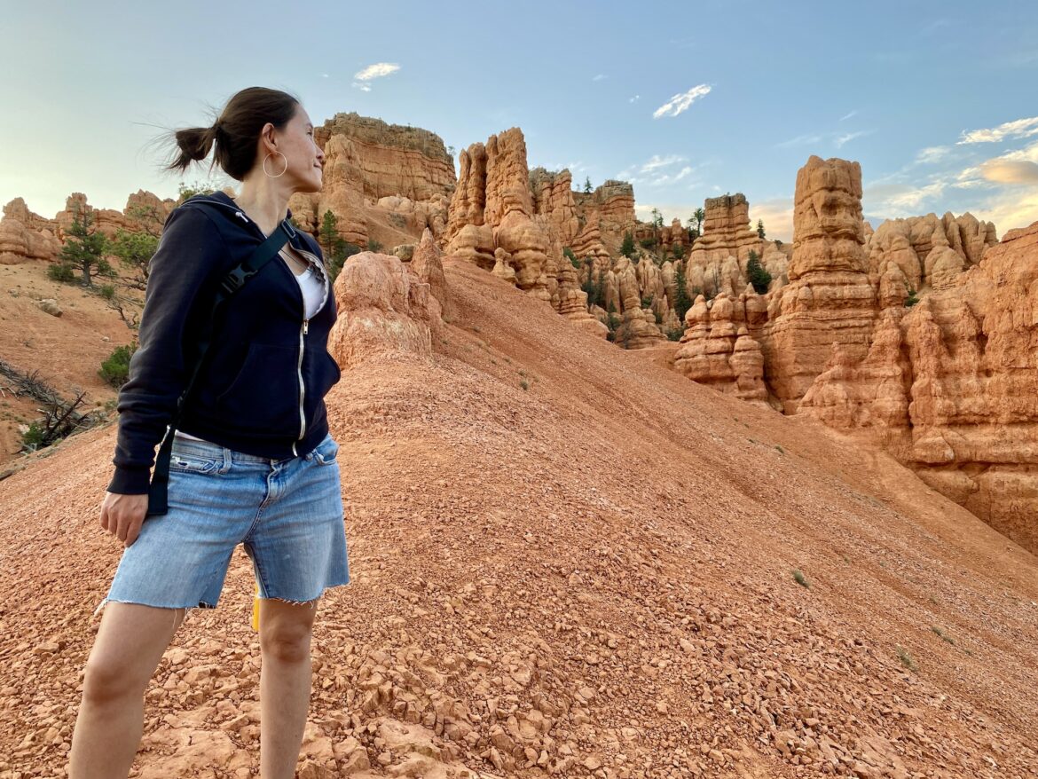 Image description: Photo of Jasmin on her sabbatical road trip, standing on a hill of desert red rocks in Utah, looking off into the distance.
